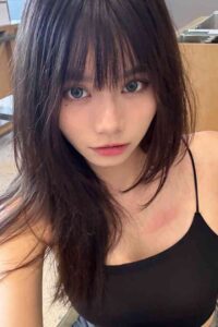 Young woman with long dark hair and bangs, wearing a black top.