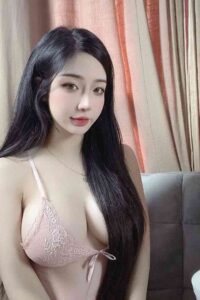 Young woman with long black hair, wearing a pink lace bralette.